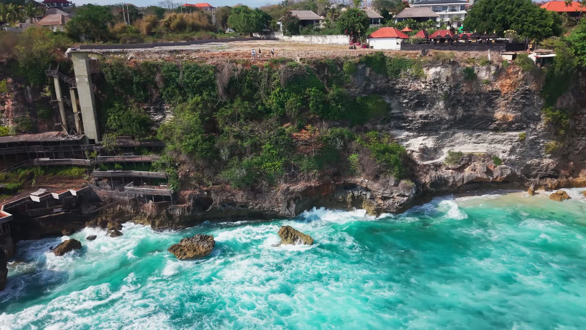 Original drone photograph of the cliff face, existing timber structures and water at the cliff base.